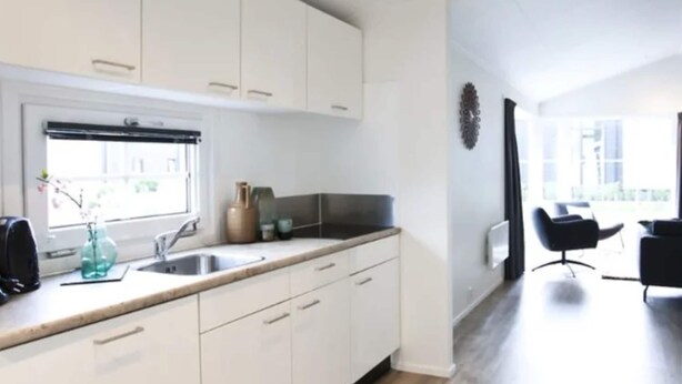 Una cocina moderna con armarios blancos, un ventanal y un comedor con una silla negra.