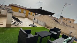 A rooftop patio with artificial grass, outdoor furniture, and a large umbrella.