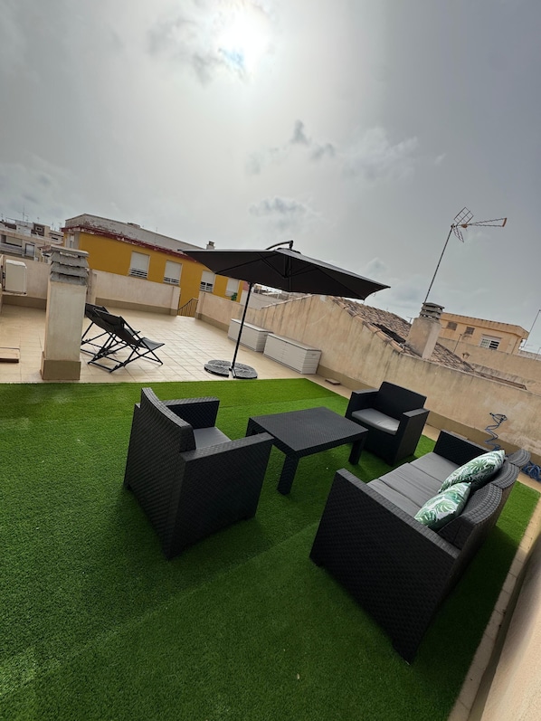 A rooftop patio with artificial grass, outdoor furniture, and a large umbrella.