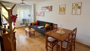 A living room with a sofa, a dining table with chairs, a ceiling fan, and wall art.