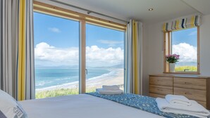 Ein Schlafzimmer mit einem großen Bett, einer Holzkommode und einem Fenster mit Blick auf Strand und Meer.