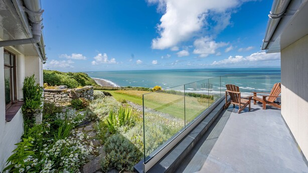 Ein Balkon mit Blick auf das Meer, eine Steinmauer und eine begrünte Fläche mit Pflanzen.