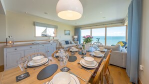Ein Essbereich mit Holztisch, gedecktem Tisch für eine Mahlzeit, einer Couch und Blick aufs Meer.
