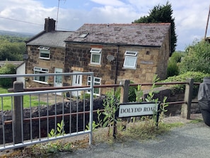 A stone house with a red roof, a metal gate, and a 'DOLYDD ROAD' sign.