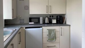 Une cuisine compacte avec des meubles blancs, un four à micro-ondes, une bouilloire, un grille-pain et une machine à café.