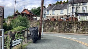 Une vue de rue avec un panneau indiquant « DOLYDD ROAD » et un bâtiment portant l’inscription « Queens Hotel ».