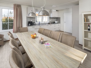 Prepare meals in the spacious kitchen with a large island, sink, and ample counter space, complemented by a dining area with a long table and comfortable seating.