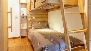 Une chambre avec un lit superposé, une échelle en bois, une petite étagère et un plancher en bois.