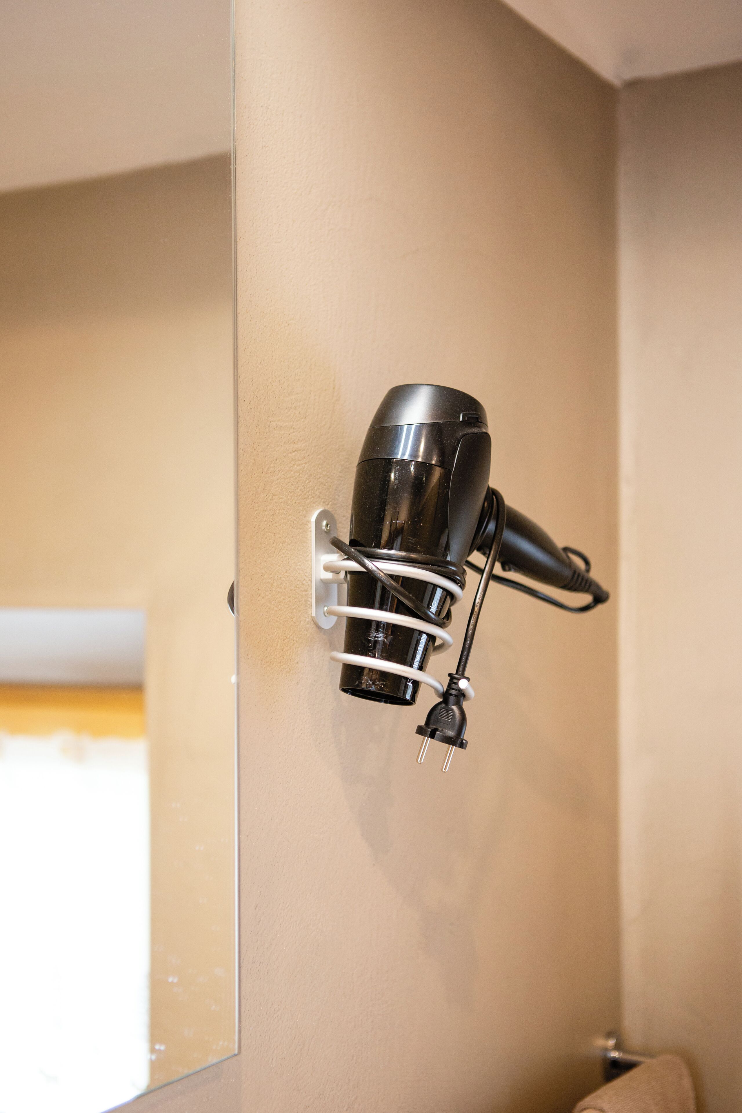 Un sèche-cheveux fixé sur un mur beige dans une salle de bain.