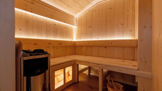 Un sauna avec des murs et des bancs en bois, un seau en bois et une poubelle.