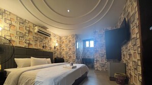 Une chambre d’hôtel avec un grand lit, un téléviseur à écran plat, un ventilateur et un papier peint à motifs.