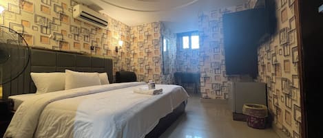A hotel room with a large bed, a flat-screen TV, a fan, and patterned wallpaper.