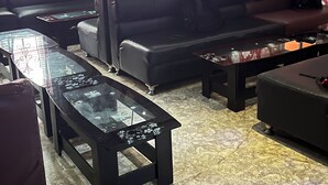 Un salon comprenant un ensemble de canapés, des tables basses avec un plateau en verre et un papier peint à motifs.