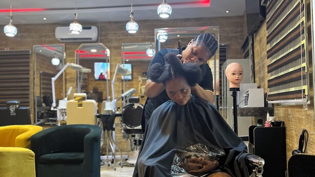 L'intérieur d'un salon de coiffure moderne, avec une cliente assise, un coiffeur qui travaille et une tête de mannequin.