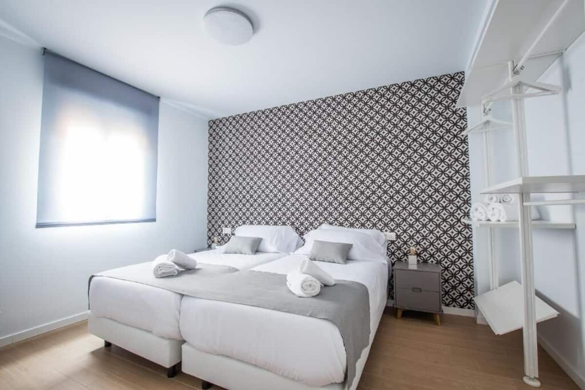 A modern hotel room with a large bed, a bedside table, a wardrobe, and a patterned wallpaper.