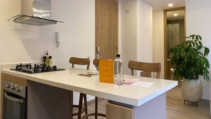 Eine moderne Küche mit weißer Arbeitsplatte, Holzstühlen, einem eingebauten Backofen und einem Blumentopf.