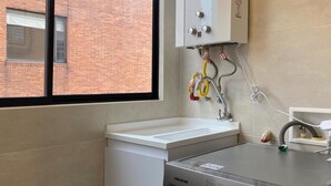 Ein kleiner Waschraum mit einer Waschmaschine, einem Waschbecken und einem Fenster mit Blick auf ein Backsteingebäude.