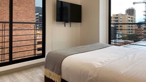 Ein Schlafzimmer mit großem Fenster, einem Bett und einem an der Wand befestigten Fernseher.