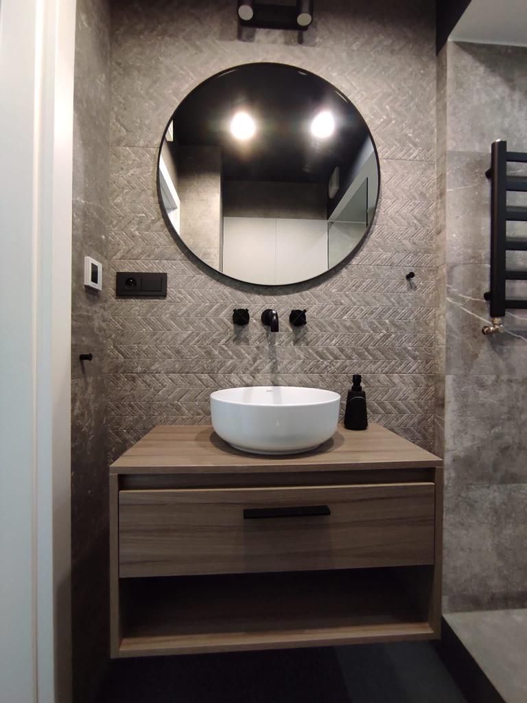 Une salle de bain avec un miroir rond, un lavabo blanc et un mur orné d’un motif en chevrons.