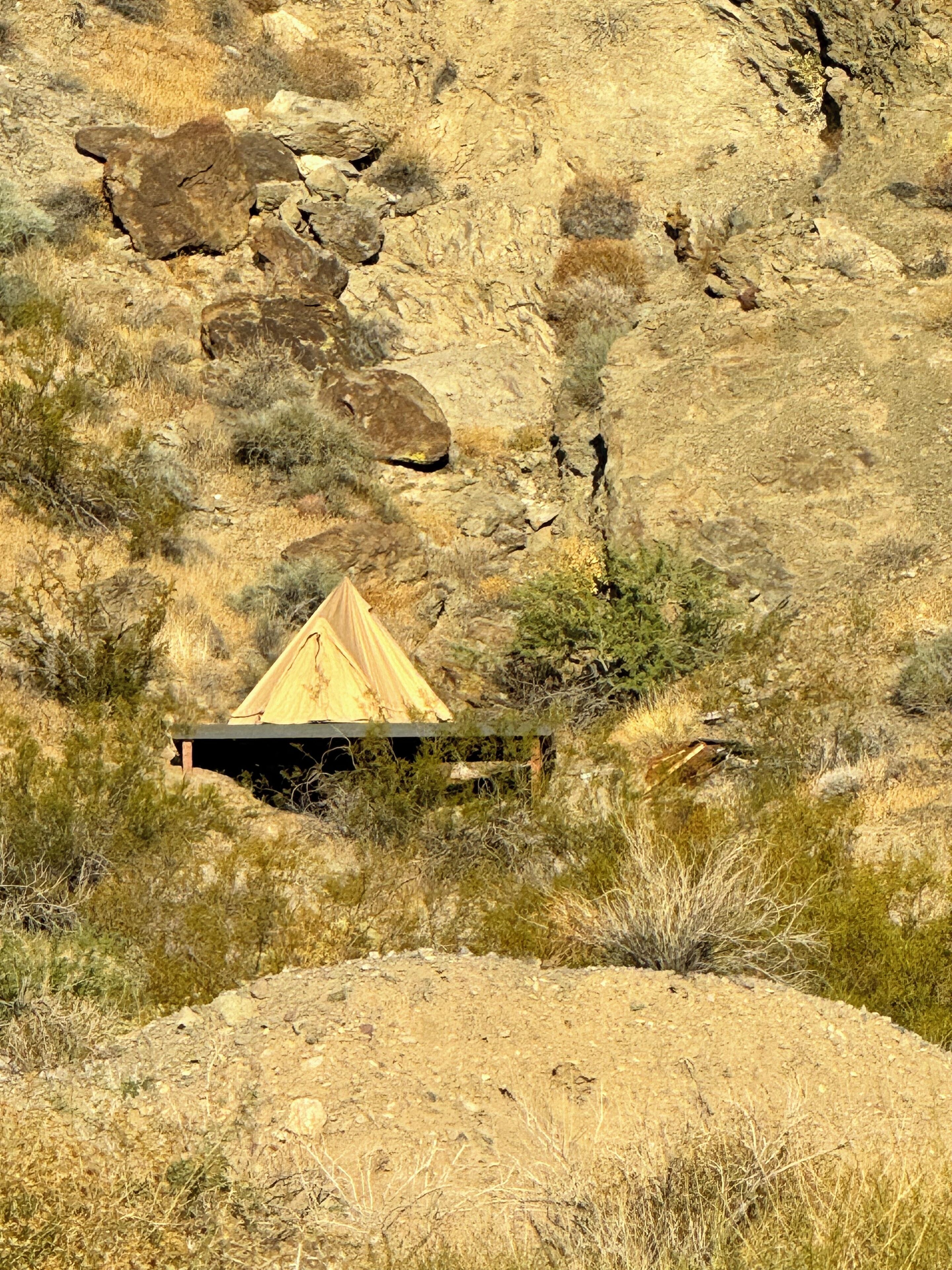 Une tente est installée sur le flanc d’une colline rocheuse où la végétation est rare.