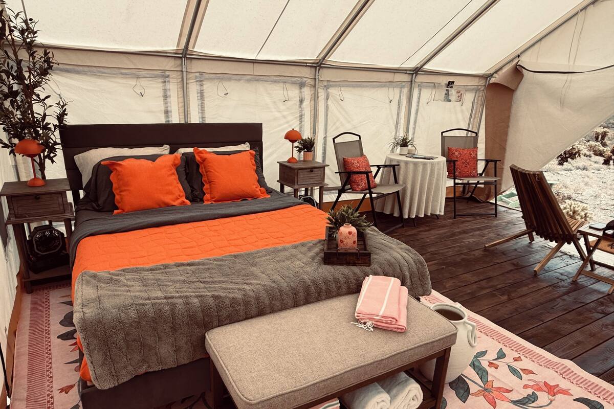 A tented accommodation with a bed, bedside tables, chairs, a small table, and a bench.
