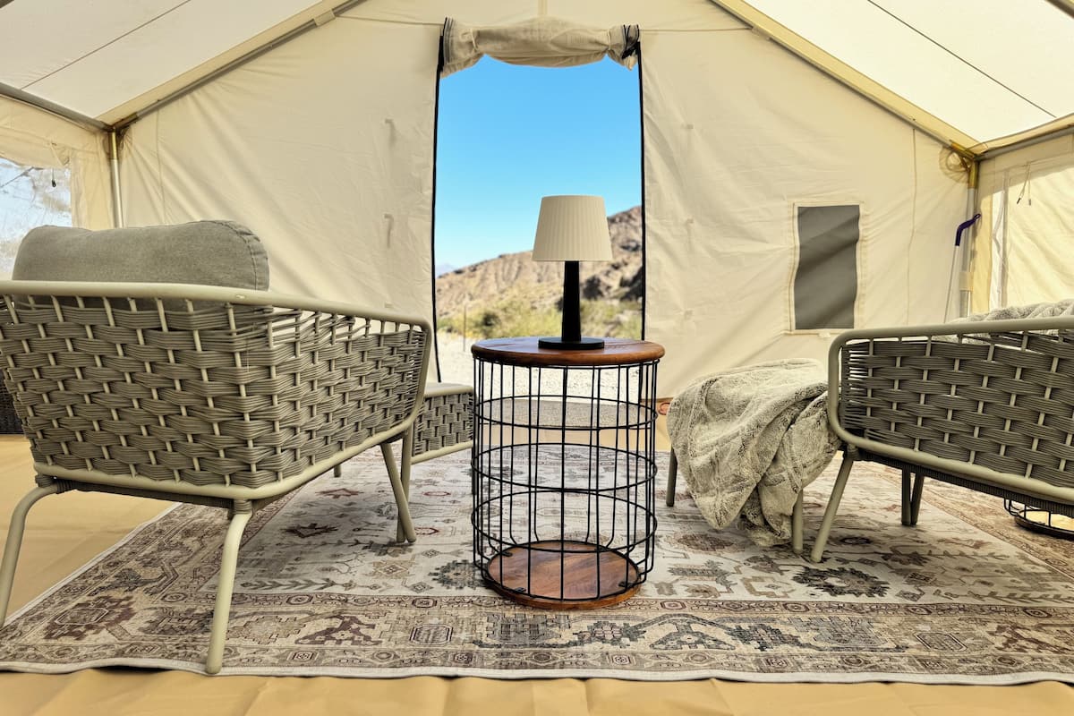 A tent with two wicker chairs, a small round table with a lamp, and a patterned rug.