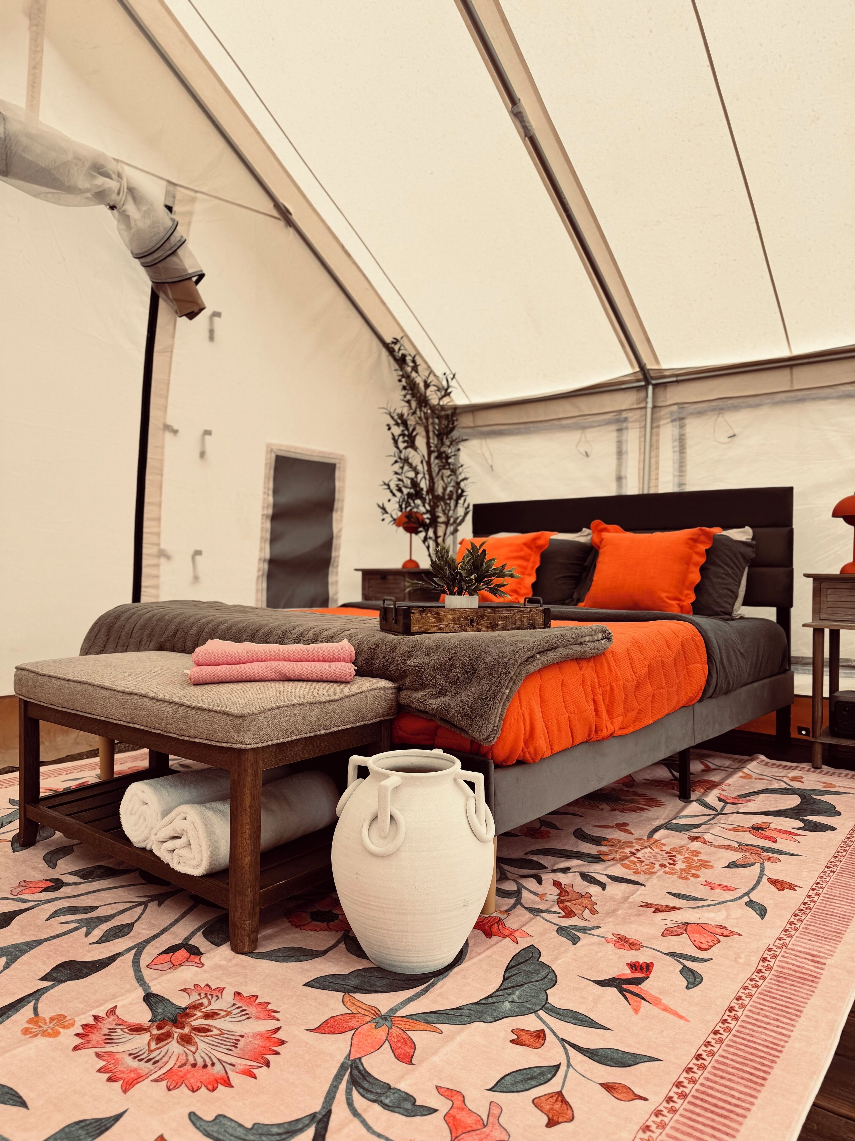 A tented room with a bed, a bench, a large vase, and a patterned rug.