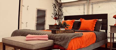 A tented room with a bed, a bench, a large vase, and a patterned rug.
