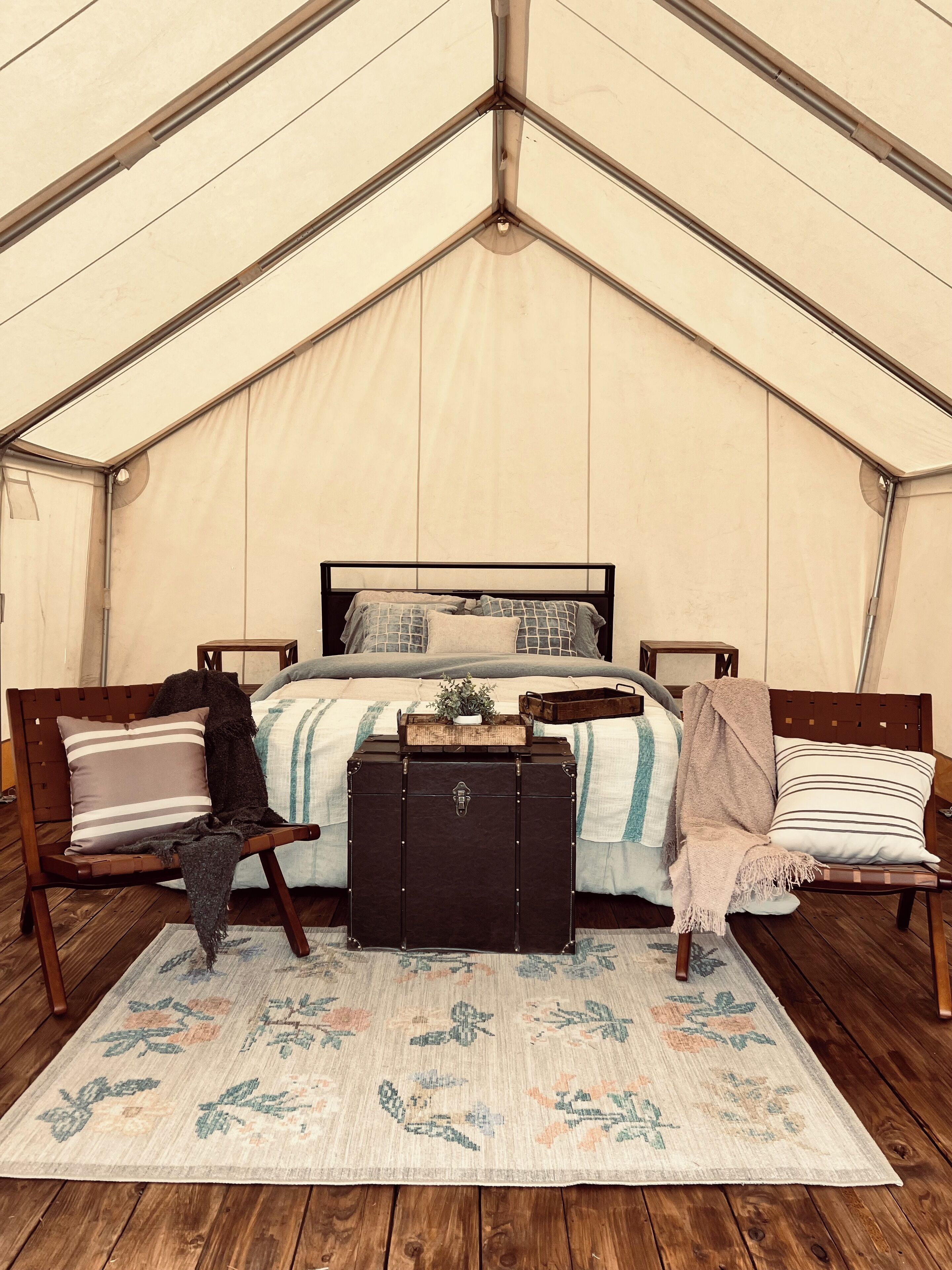 A tented room with a bed, two chairs, a chest of drawers, and a patterned rug.