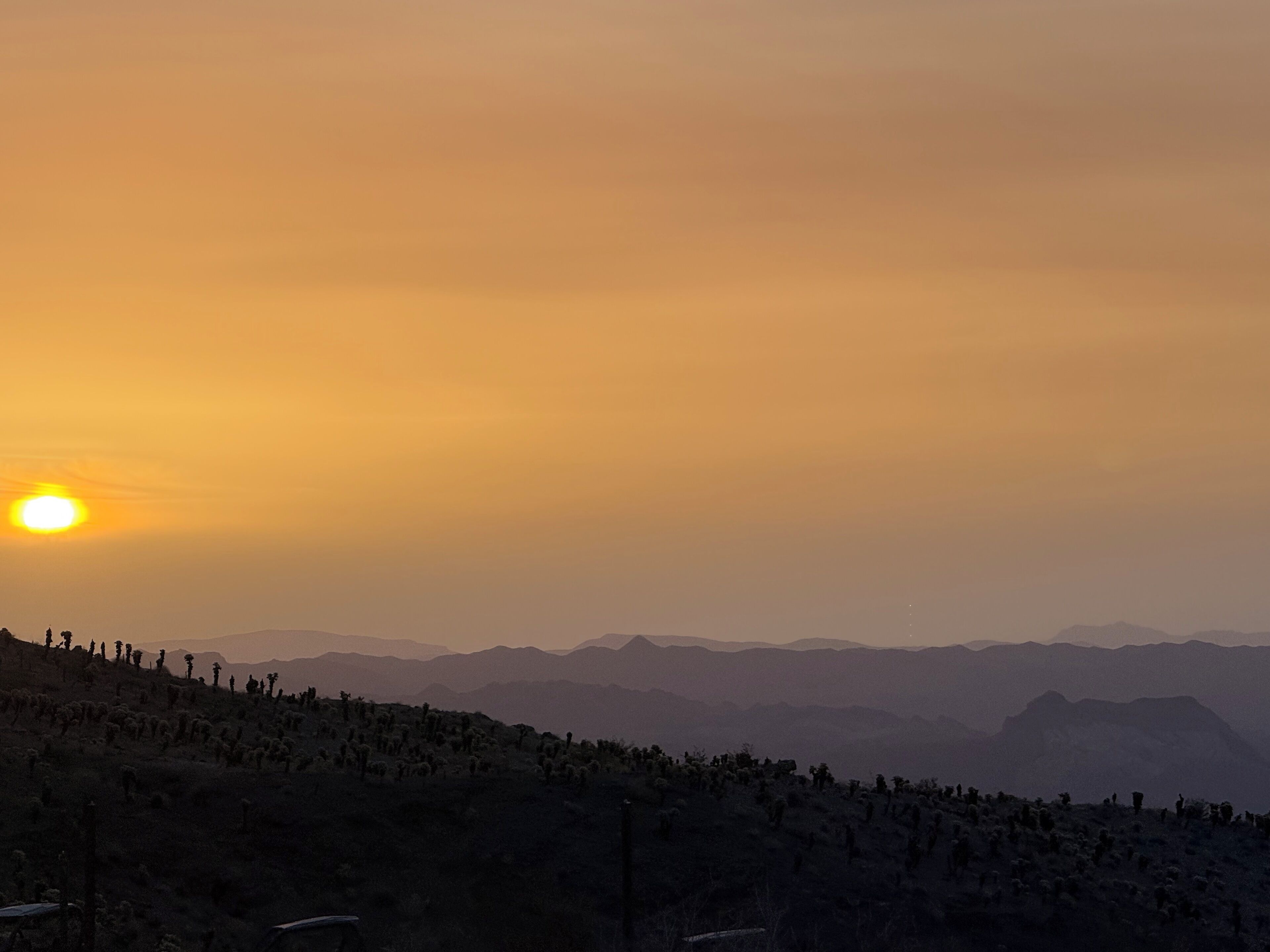 Un paysage désertique avec un coucher de soleil, des montagnes lointaines et une végétation clairsemée.