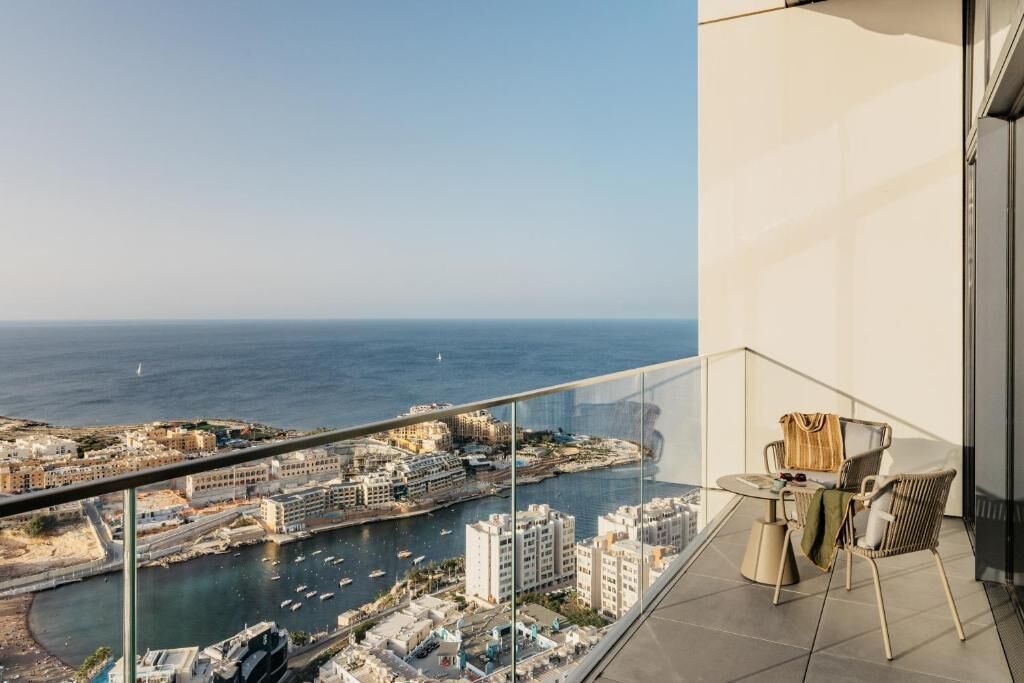 Un balcón con barandilla de vidrio que ofrece vistas a una ciudad costera con edificios y barcos.