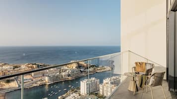 Un balcón con barandilla de vidrio que ofrece vistas a una ciudad costera con edificios y barcos.