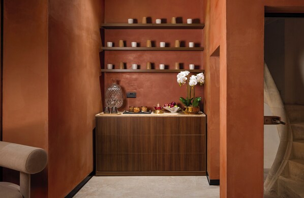 A narrow hallway with a wooden reception desk, shelves with small containers, a vase with white flowers, and a glass bottle. - ME Malta by Meliá (St. Julian's)