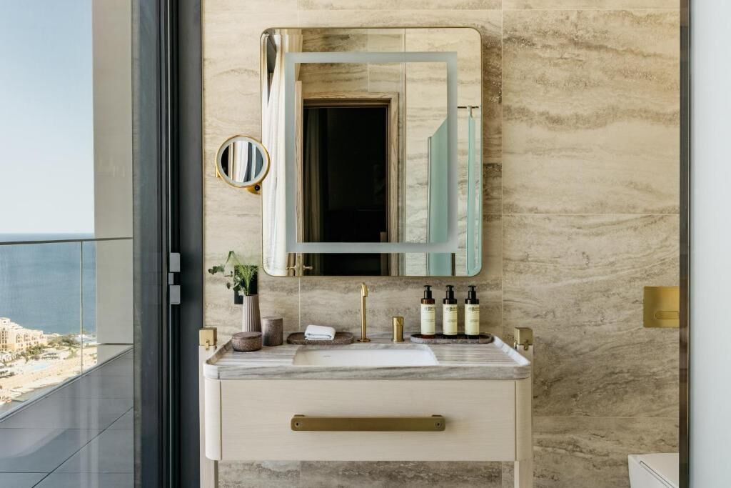 Une salle de bain moderne avec un meuble-lavabo en marbre, un grand miroir et une vue sur la plage.