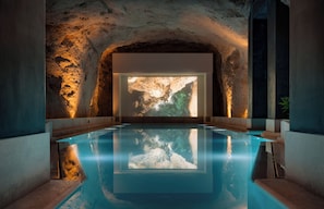 Una piscina con una gran pantalla proyectando una escena natural, rodeada de muros de piedra.