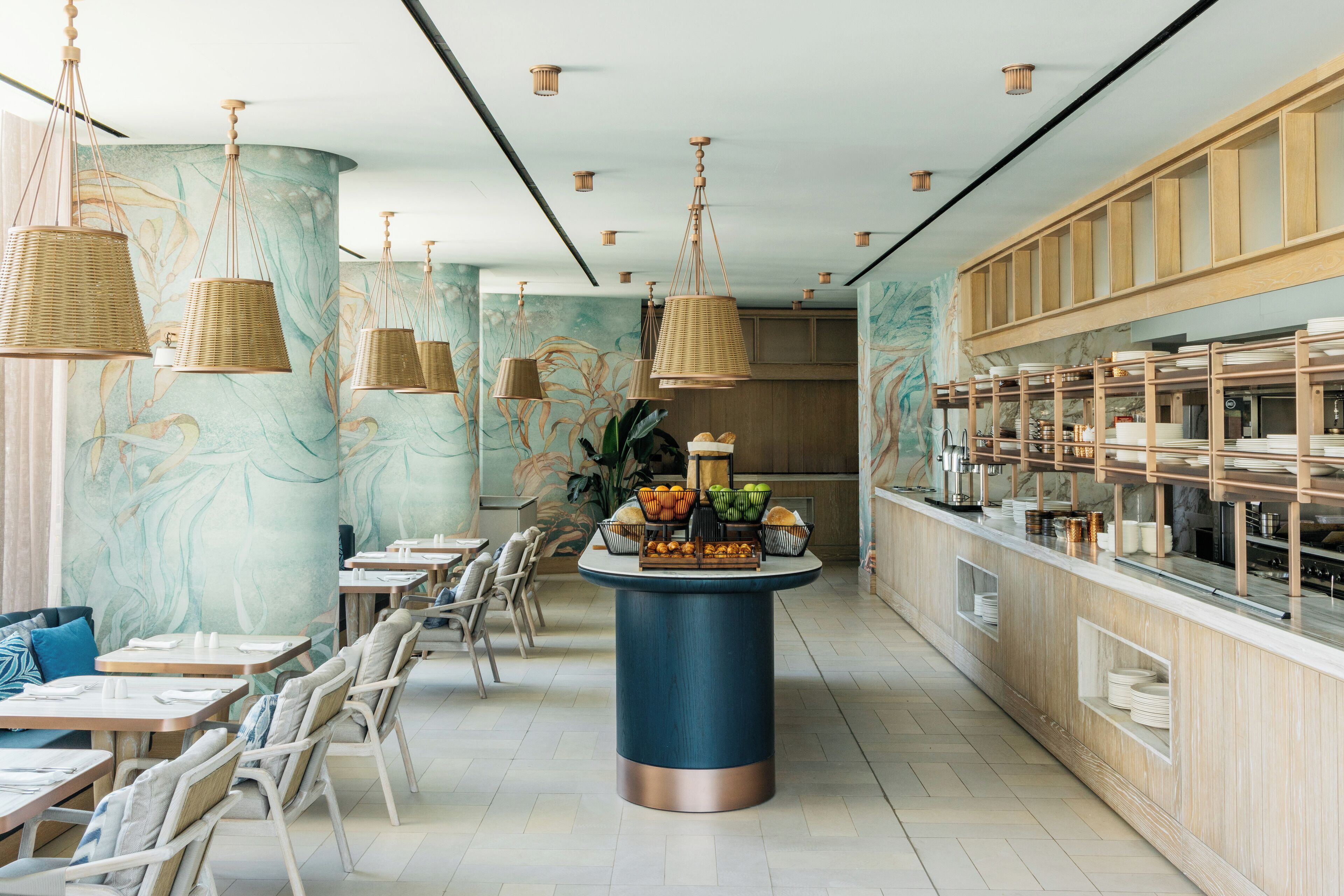 A restaurant with a long counter, wicker hanging lights, and a central fruit display.