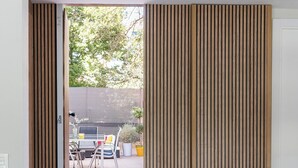 Un salon moderne avec un canapé gris, une petite table blanche et une porte-fenêtre coulissante donnant sur une terrasse extérieure avec une table et des chaises.