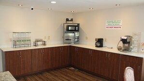 A kitchen with wooden cabinets, a microwave, and a coffee maker. There is a sign on the wall that says "Please do not carry breakfast back to room" and "Do not waste."