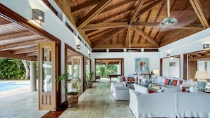 A spacious living area with a high ceiling and wooden beams, a pool visible through the open door, and a comfortable seating arrangement. - Gorgeous Villa at Casa de Campo With Large Pool Chef Maid and 2 Golf Carts (La Romana)