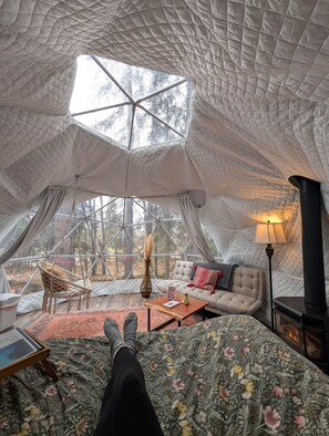 A cozy interior with a sofa, a wooden coffee table, and a hanging chair, all under a large, geometric ceiling structure.