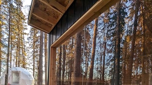 Eine Holzhütte mit einem großen Fenster, einem Kamin aus Stein und einem bewaldeten Gebiet im Hintergrund, in dem ein Zelt steht.