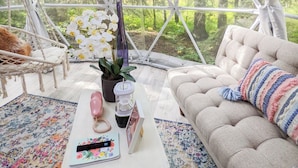 Ein gemütlicher, geometrisch gestalteter Innenraum mit einer Couch, einem kleinen Tisch mit Fernbedienung, einer Topfpflanze und einem Hängesessel.