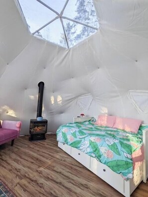 A cozy tent-style room with a bed, a sofa, and a wood-burning stove. - The Aspen Geodome (Alberta Beach)