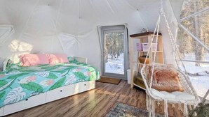 A cozy, tent-like bedroom with a bed, a hanging chair, and a wooden shelf.