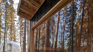 A cabin with a large window, a stone fireplace, and a forested area with a tent in the background.