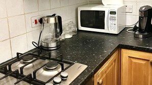 Una cocina con gabinetes de madera, estufa a gas, microondas, cafetera y hervidor.