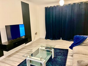 A modern living room with a flat-screen TV, a glass coffee table, and a sofa.
