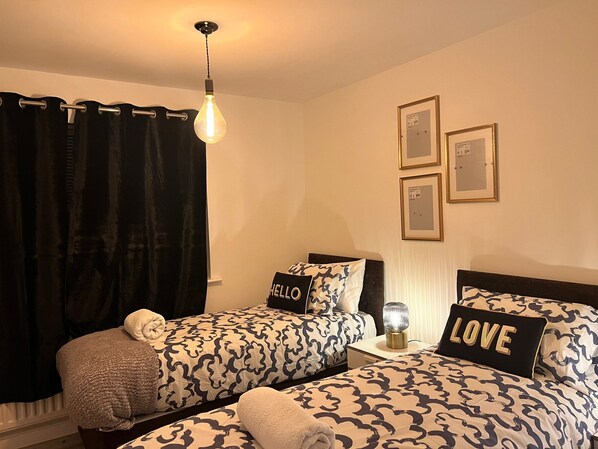 A bedroom with two beds, a nightstand, a lamp, and a curtain.