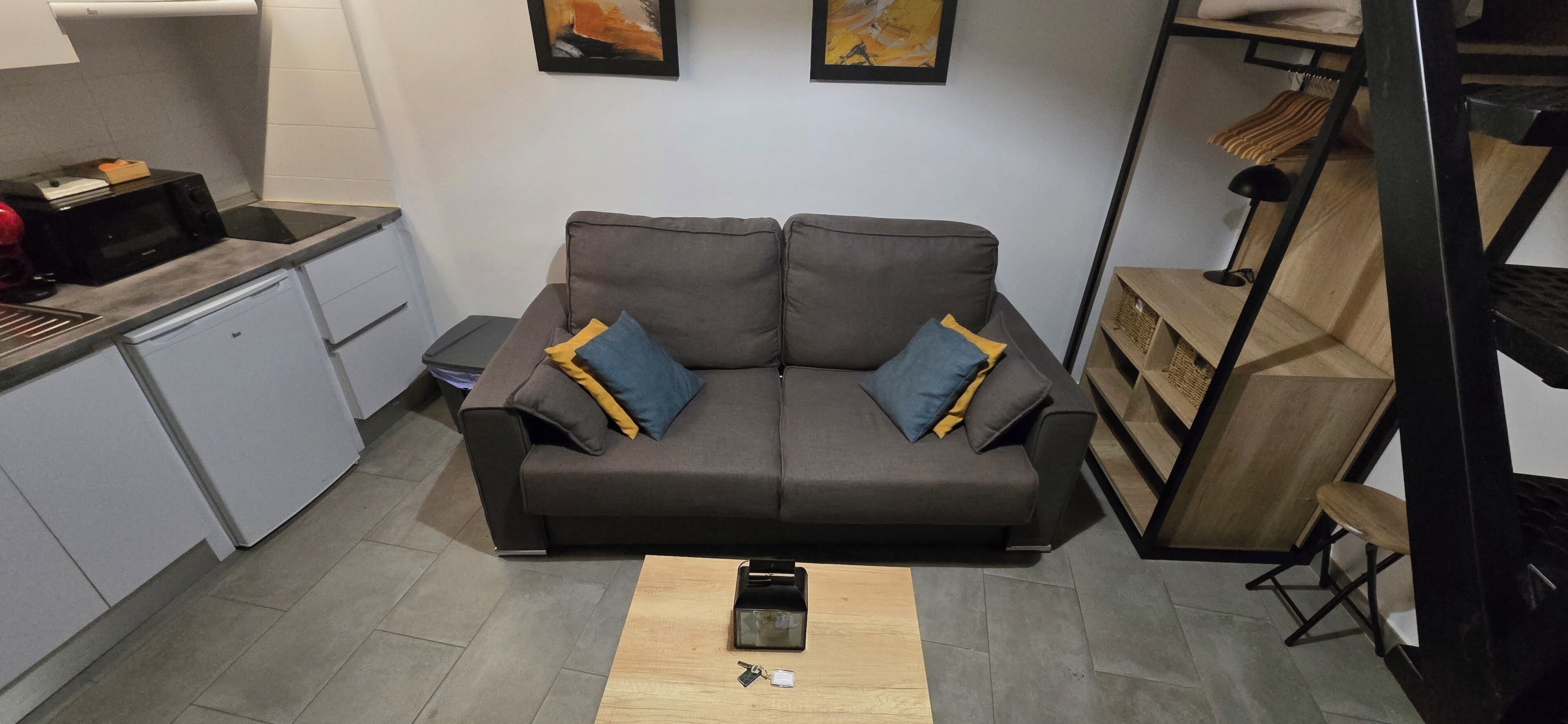 Un salon moderne avec un canapé gris, une petite table basse et un coin cuisine équipé d’un four à micro-ondes et de placards.