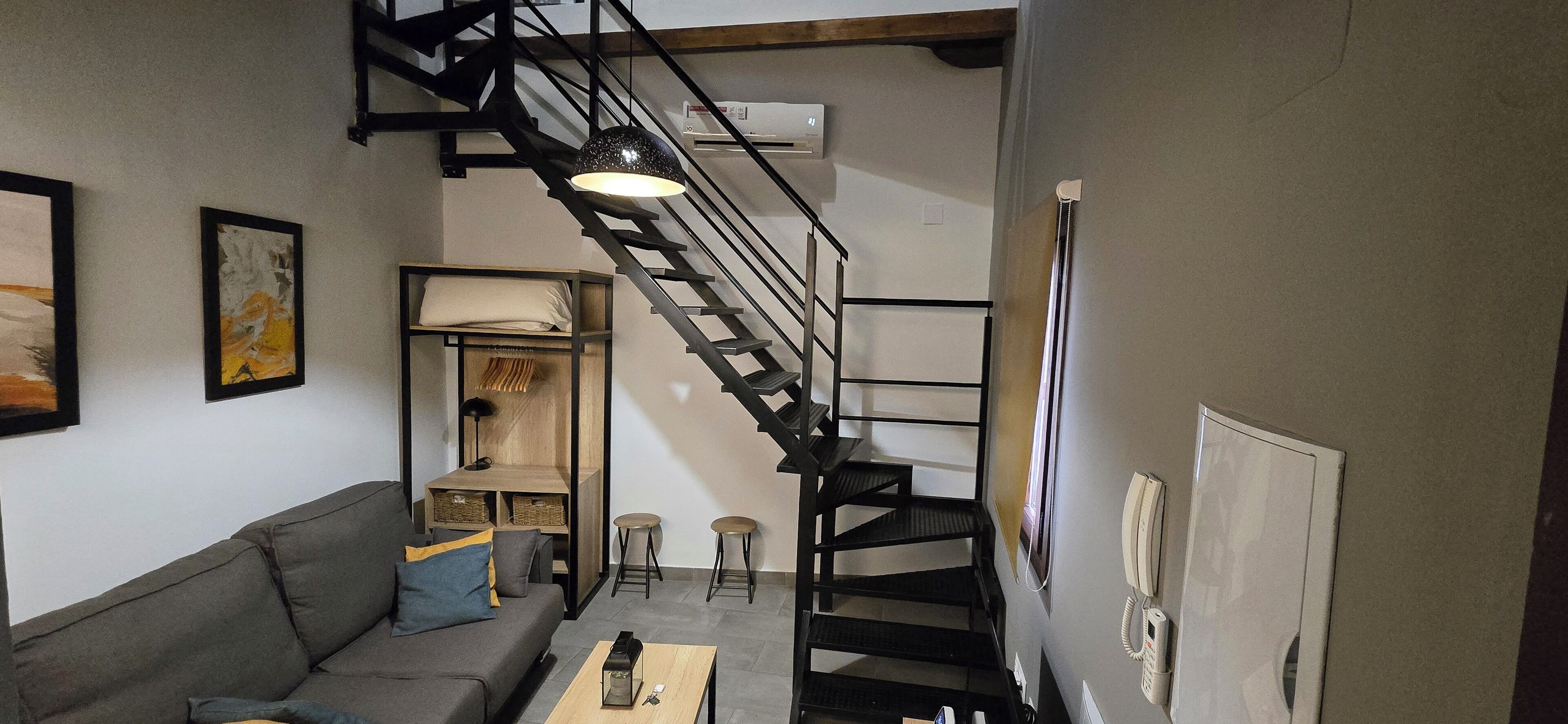 A modern living room with a grey sofa, a wooden coffee table, and a black spiral staircase.